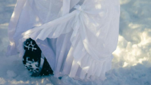 A woman wearing a dress walks in boots in the snow