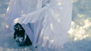 A woman wearing a dress walks in boots in the snow