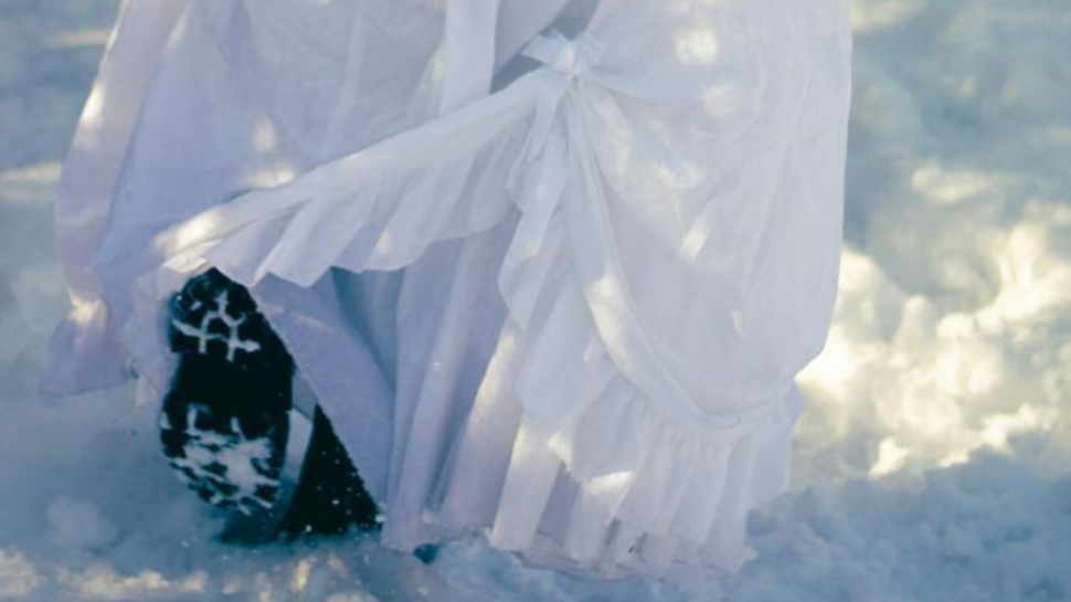 A woman wearing a dress walks in boots in the snow